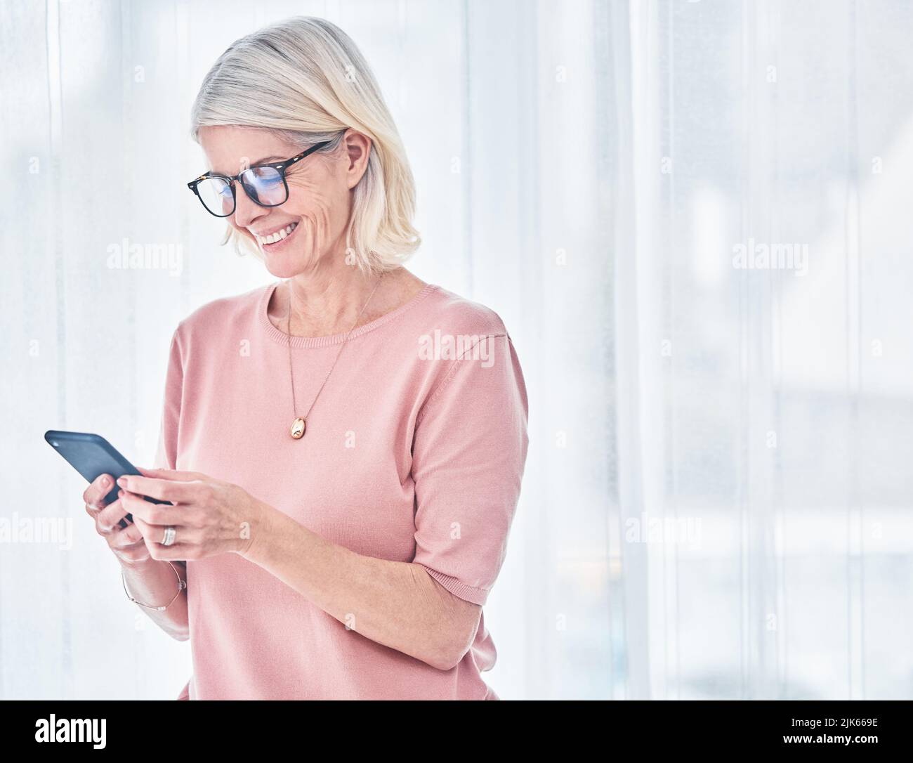 Glück ist nur ein Fingertipp. Eine ältere Frau benutzt ihr Handy zu Hause. Stockfoto