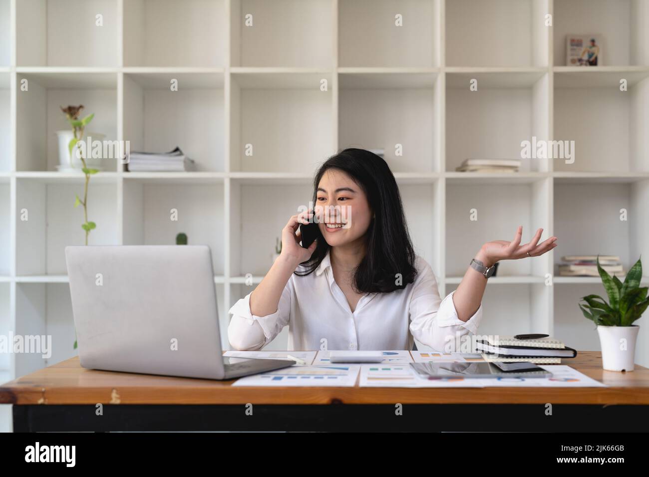 Junge asiatische Frau, die im Büro auf dem Mobiltelefon spricht. Lächelnde Geschäftsfrau, die einen Anruf macht. Stockfoto