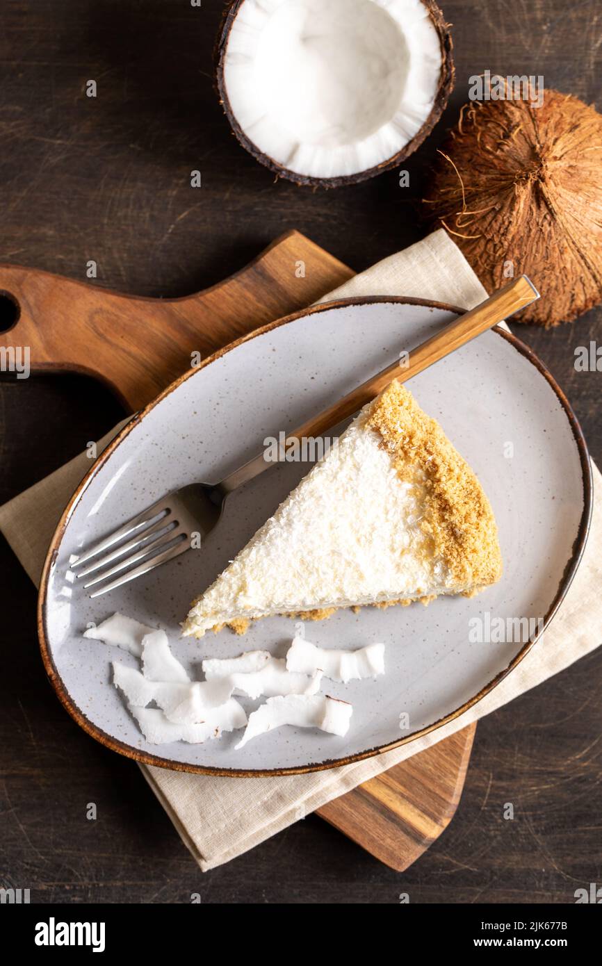 Stück Kokosnuss-Käsekuchen auf einem Teller mit frischer Kokosnuss. Stockfoto