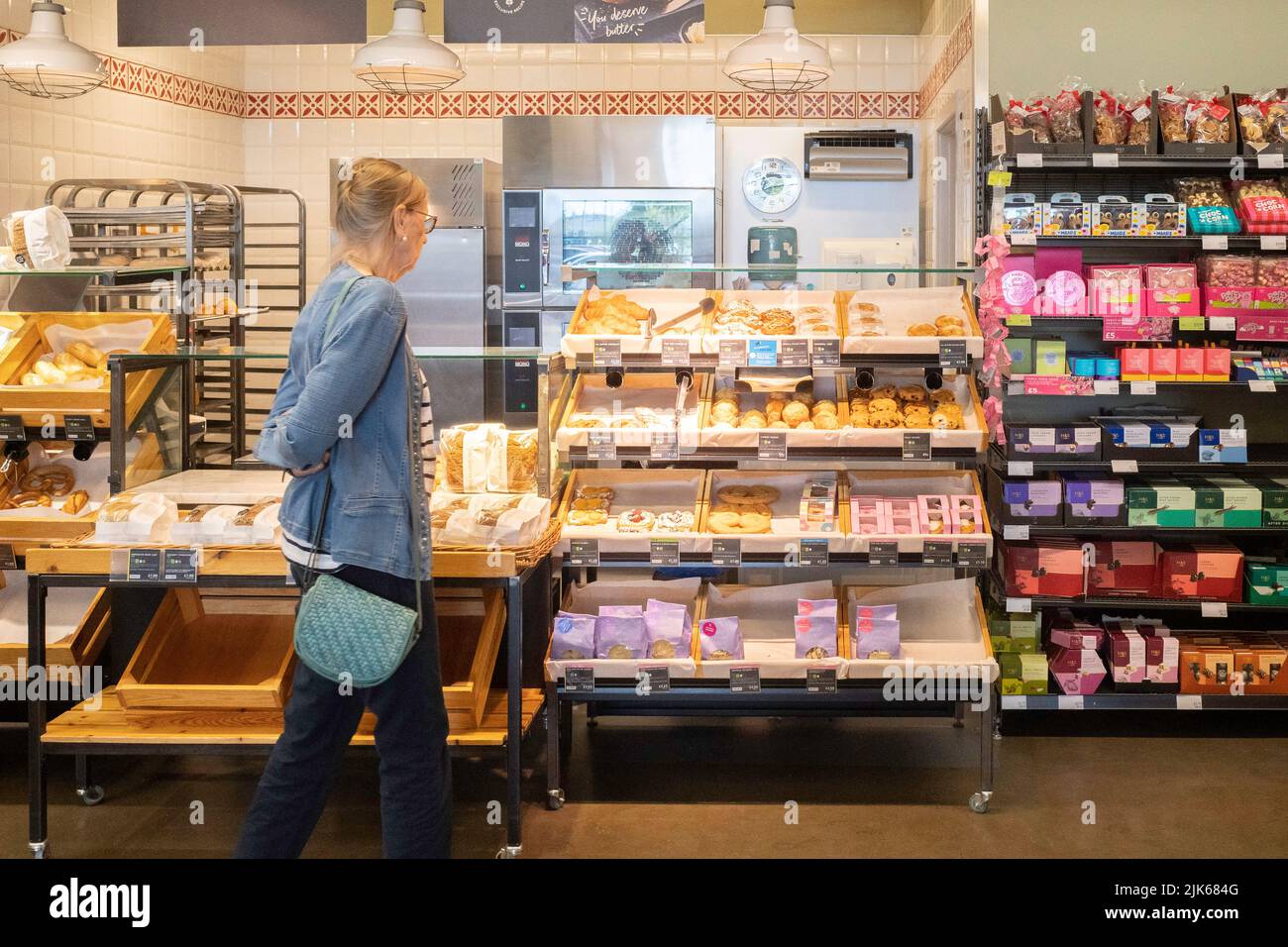 Eine ältere Frau, die Brot und Kuchen in einer M&S Food Hall auswählt und kauft Stockfoto