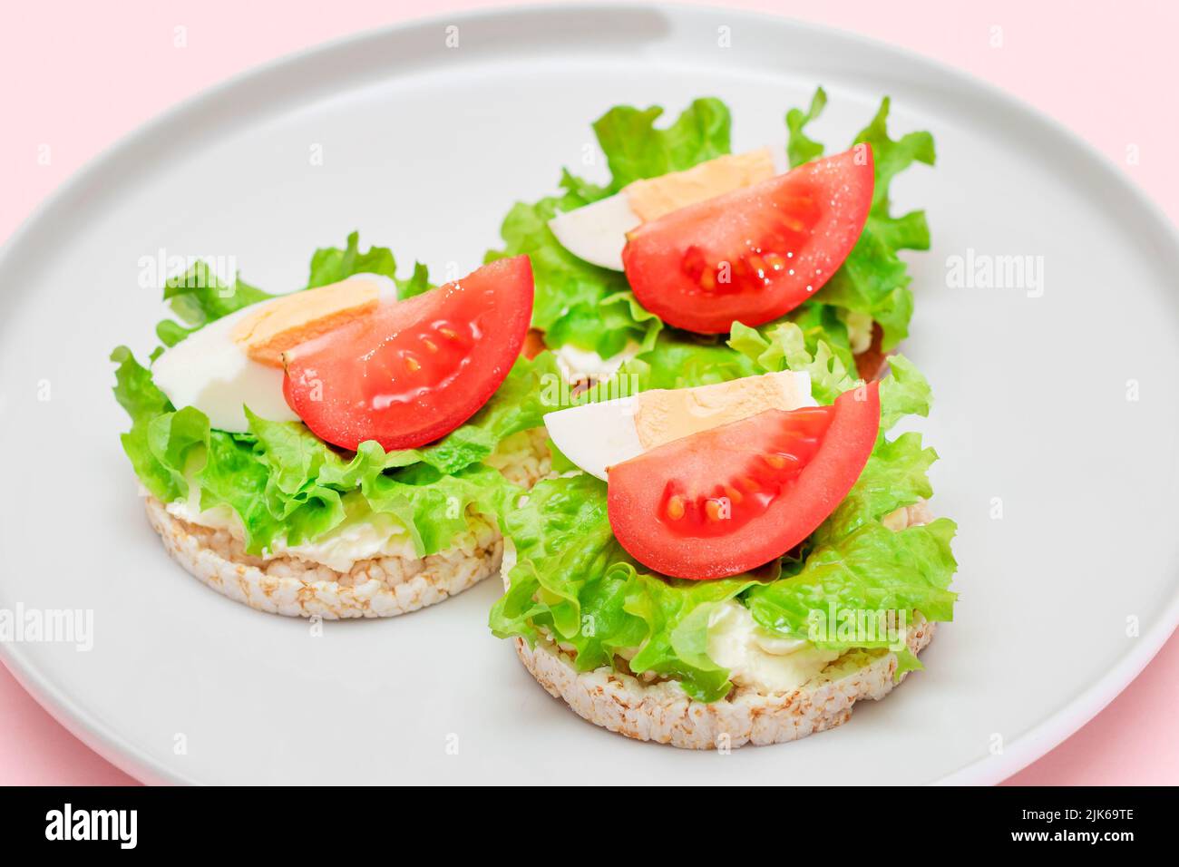 Reiskuchen-Sandwiches mit Tomaten, Salat und Ei auf weißem Teller. Einfaches Frühstück. Diät-Essen. Schnelle und gesunde Sandwiches. Knäckebrot mit leckerer Füllung. Gesunder Ernährungs-Snack Stockfoto