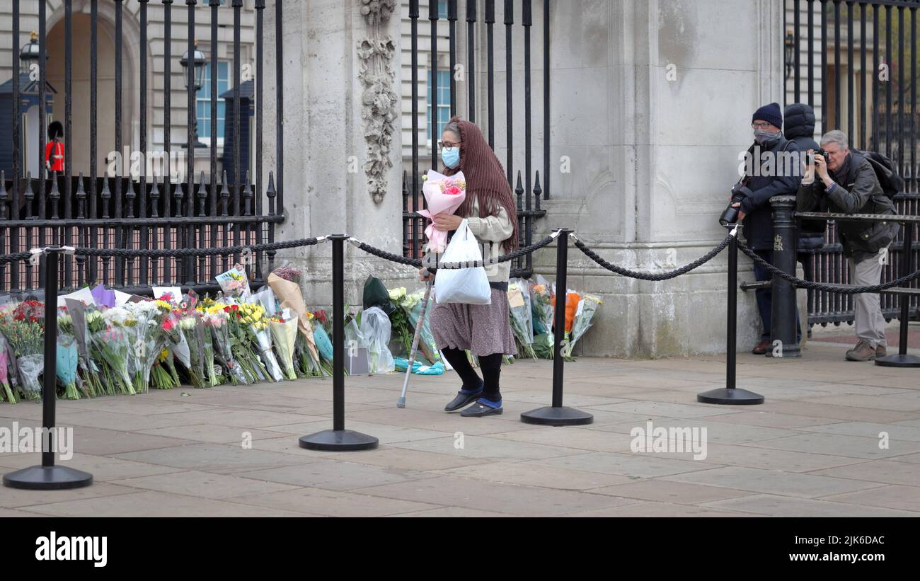 London, Großbritannien - 10. April 2021: Ältere Frau legt Blumen für den Tod von Prinz Philip, dem Herzog von Edinburgh, im Buckingham Palace in London Stockfoto