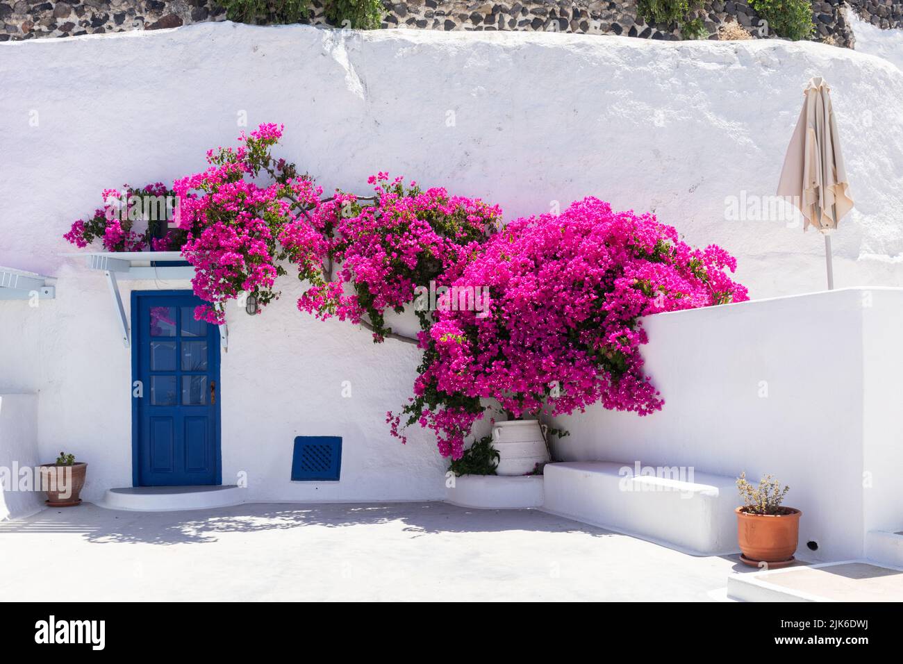 Malerische, weiß getünchte Unterkunft mit blauer Tür und leuchtend blühenden Bougainvillea, Aghios Artemios Traditional Houses, Santorini, Griechenland, EU Stockfoto