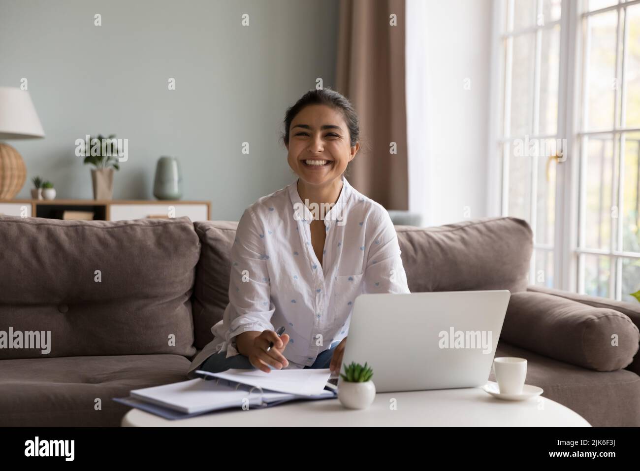 Glückliche junge indische Frau, die von zu Hause aus am Laptop arbeitet Stockfoto