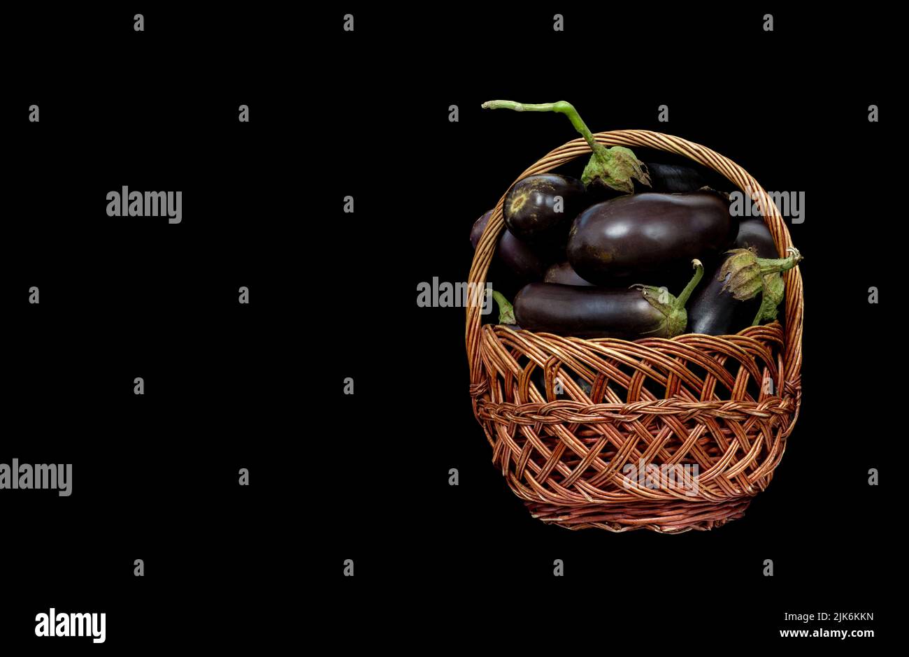 Bild eines Weidenkorbes mit Auberginen-Ernte auf schwarzem Hintergrund Stockfoto