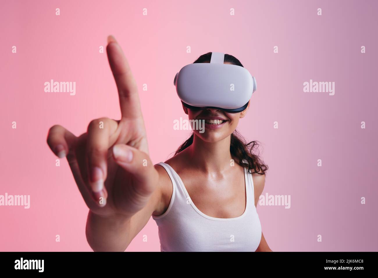 Glückliche junge Frau berührt virtuellen Raum mit ihrem Finger in einem Studio. Junge Frau lächelt fröhlich, während sie ein Virtual-Reality-Headset trägt. Sorglos Stockfoto