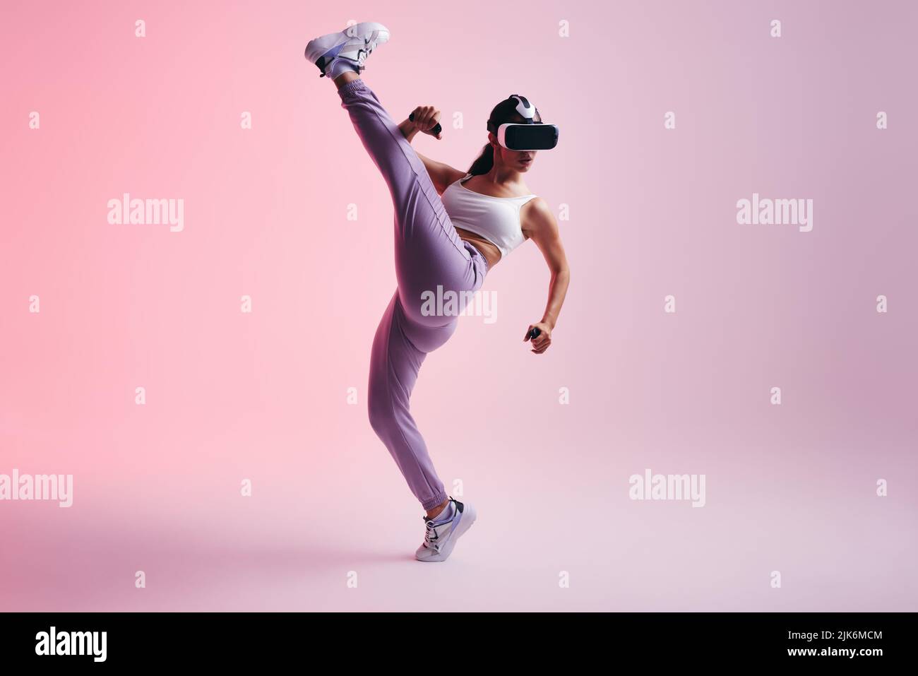 Weibliche Gamer werfen einen Kick in einem immersiven Virtual-Reality-Spiel. Aktive junge Frau, die mit Virtual-Reality-Brillen und Controllern Spiele. Energisch y Stockfoto