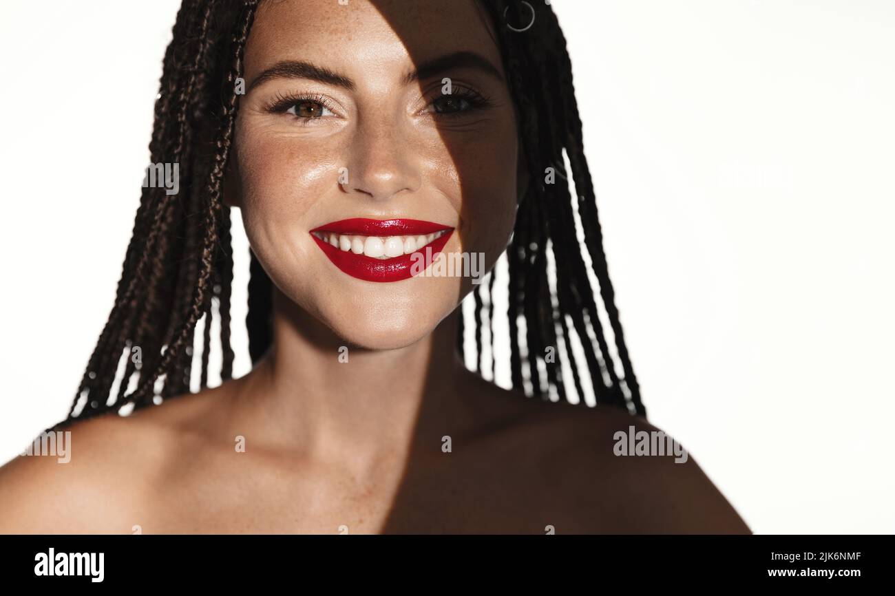 Schöne lächelnde Modelin, Frau mit rotem Lippenstift und weißem Lächeln, hat Schatten auf der Hälfte des Gesichts, steht über Studio-Hintergrund Stockfoto