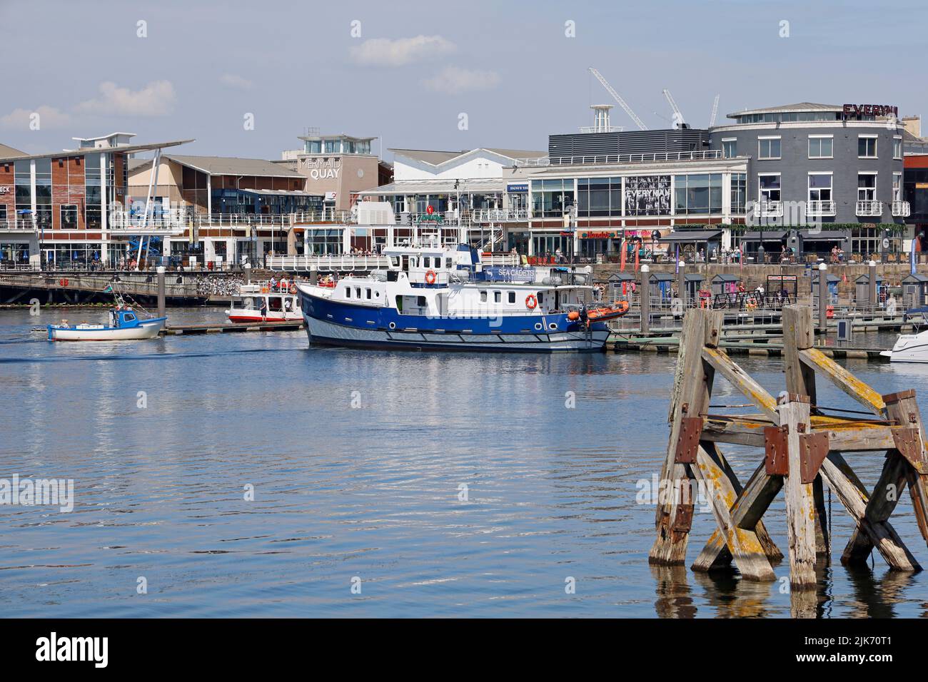 Cardiff Bay mit einem Boot der Seekadetten, das an einem Ponton festgemacht ist. Eine alte Holzankeranlage, Delfin genannt, im Vordergrund. Aufgenommen Am 2022. August. Sommer Stockfoto