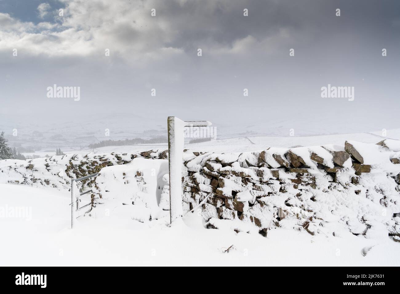 Trockenmauern und Wegweiser mit Schneeverwehungen bedeckt, Wensleydale, North Yorkshire, Großbritannien. Stockfoto