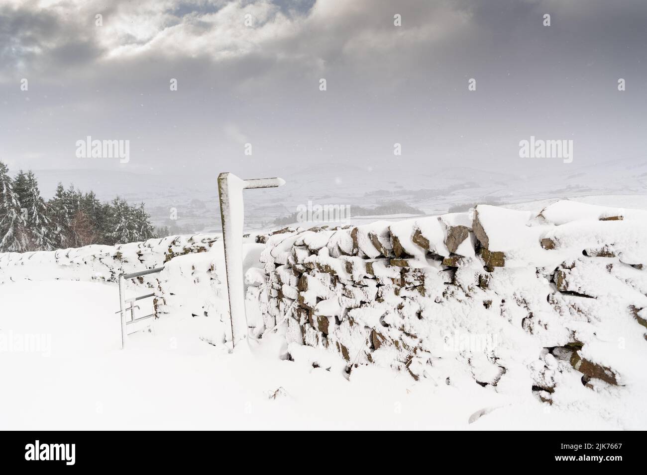 Trockenmauern und Wegweiser mit Schneeverwehungen bedeckt, Wensleydale, North Yorkshire, Großbritannien. Stockfoto