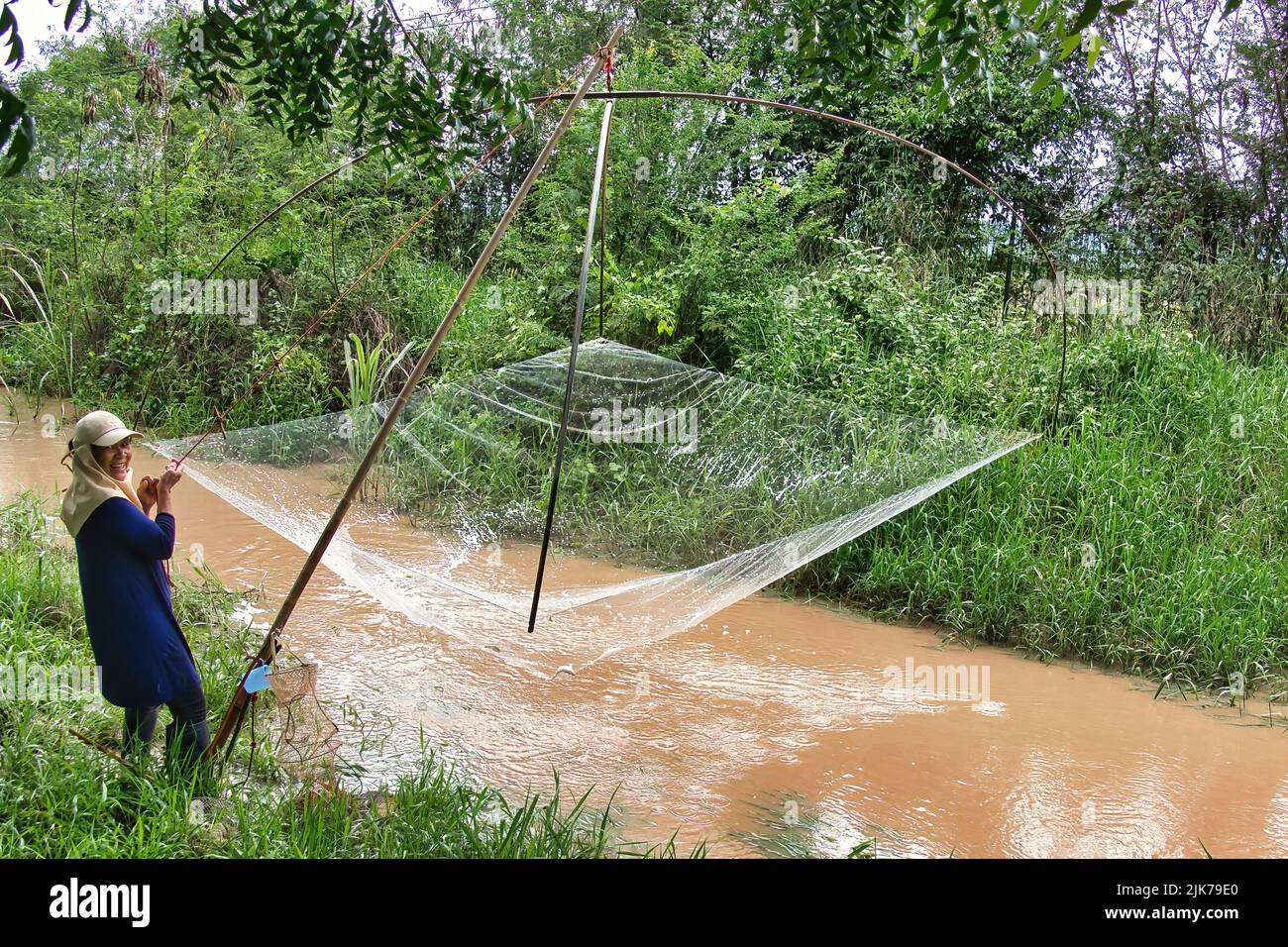 Frau, die mit einem traditionellen Fischernetz in einem kleinen Fluss, Thailand, fischt Stockfoto