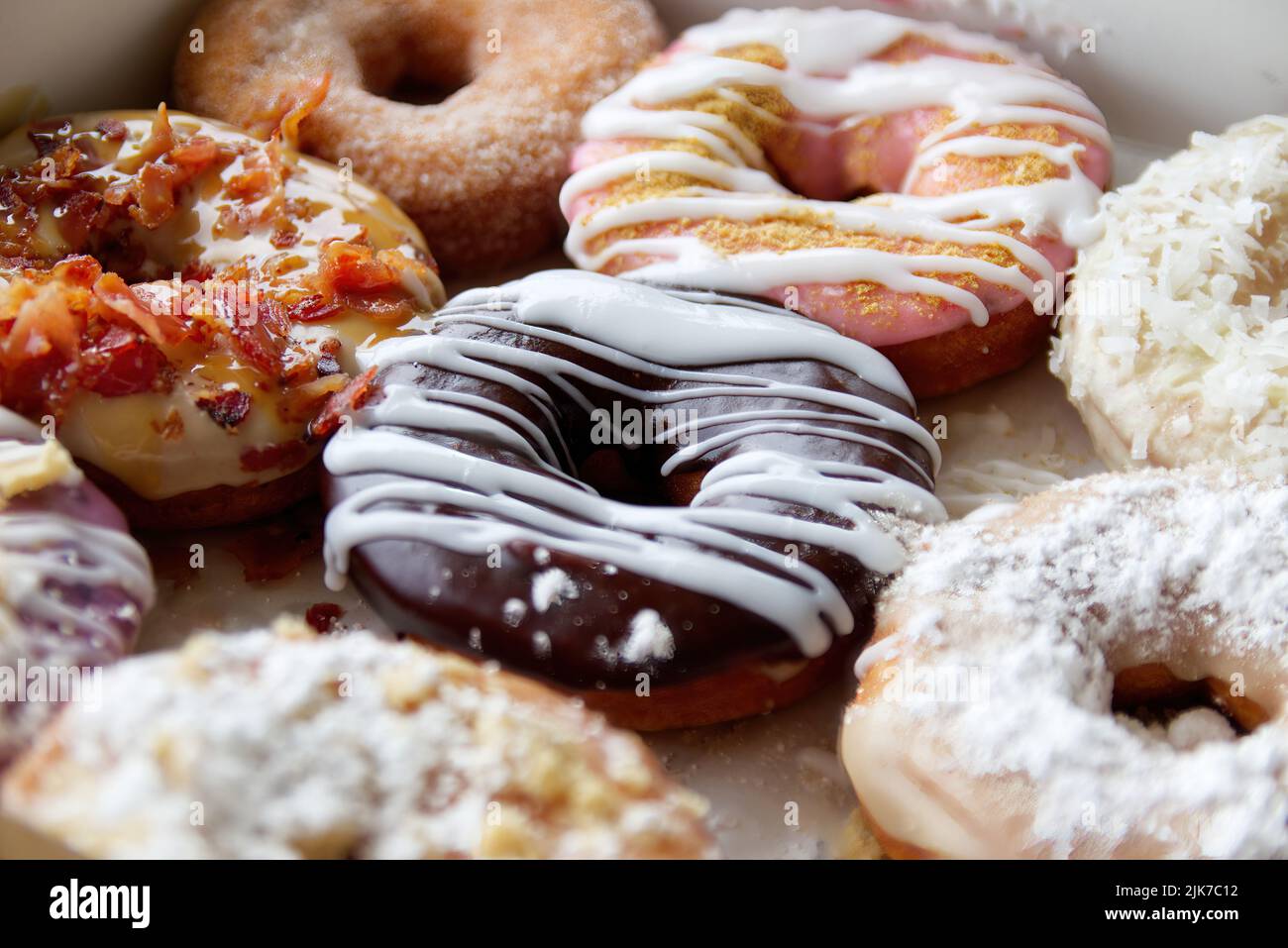 Verschiedene Donuts in einer Schachtel mit Milchschokolade, Puderpulver und Streuseln. Stockfoto