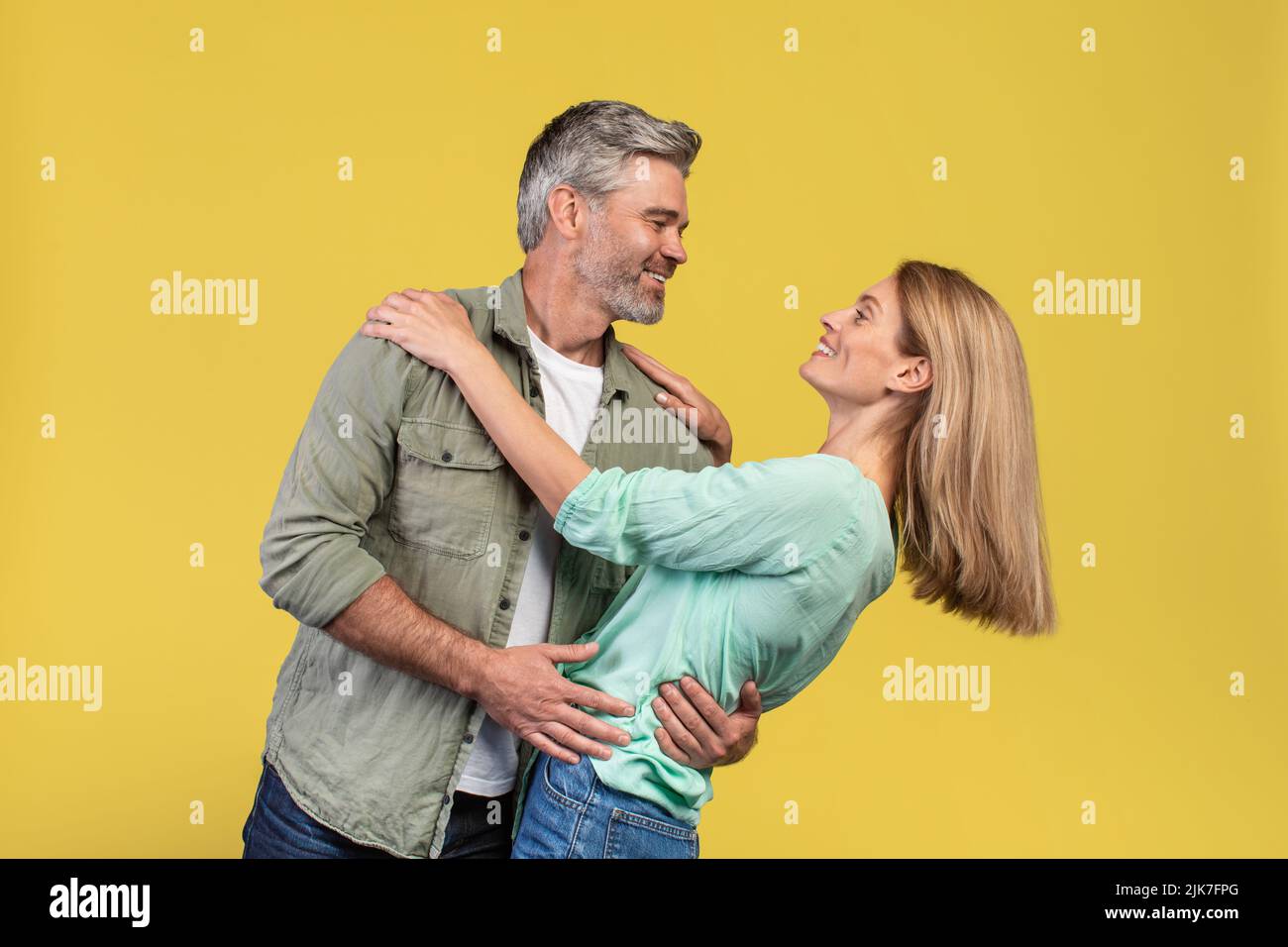 Liebende Frau mittleren Alters und ihr Mann tanzen und Spaß haben auf gelben Studio-Hintergrund Stockfoto