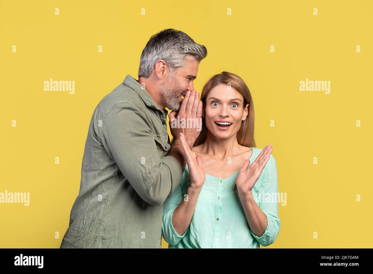 Mann mittleren Alters teilt Geheimnis oder flüstern Klatsch in das Ohr seiner Frau, Ehegatten teilen schockierende Nachrichten Stockfoto
