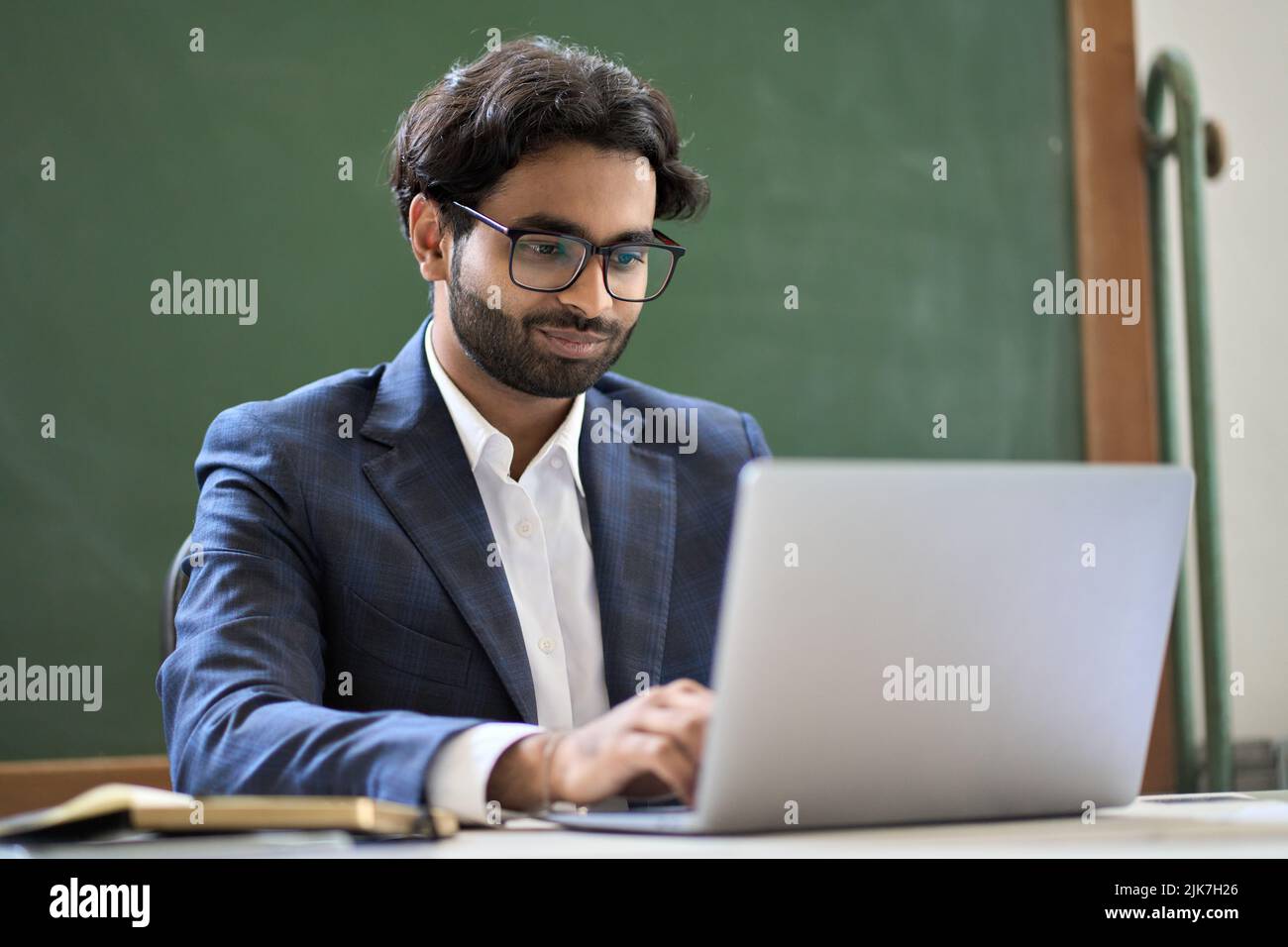 Junger indischer Geschäftsmann im Anzug, der an einem Laptop im Büro sitzt. Stockfoto