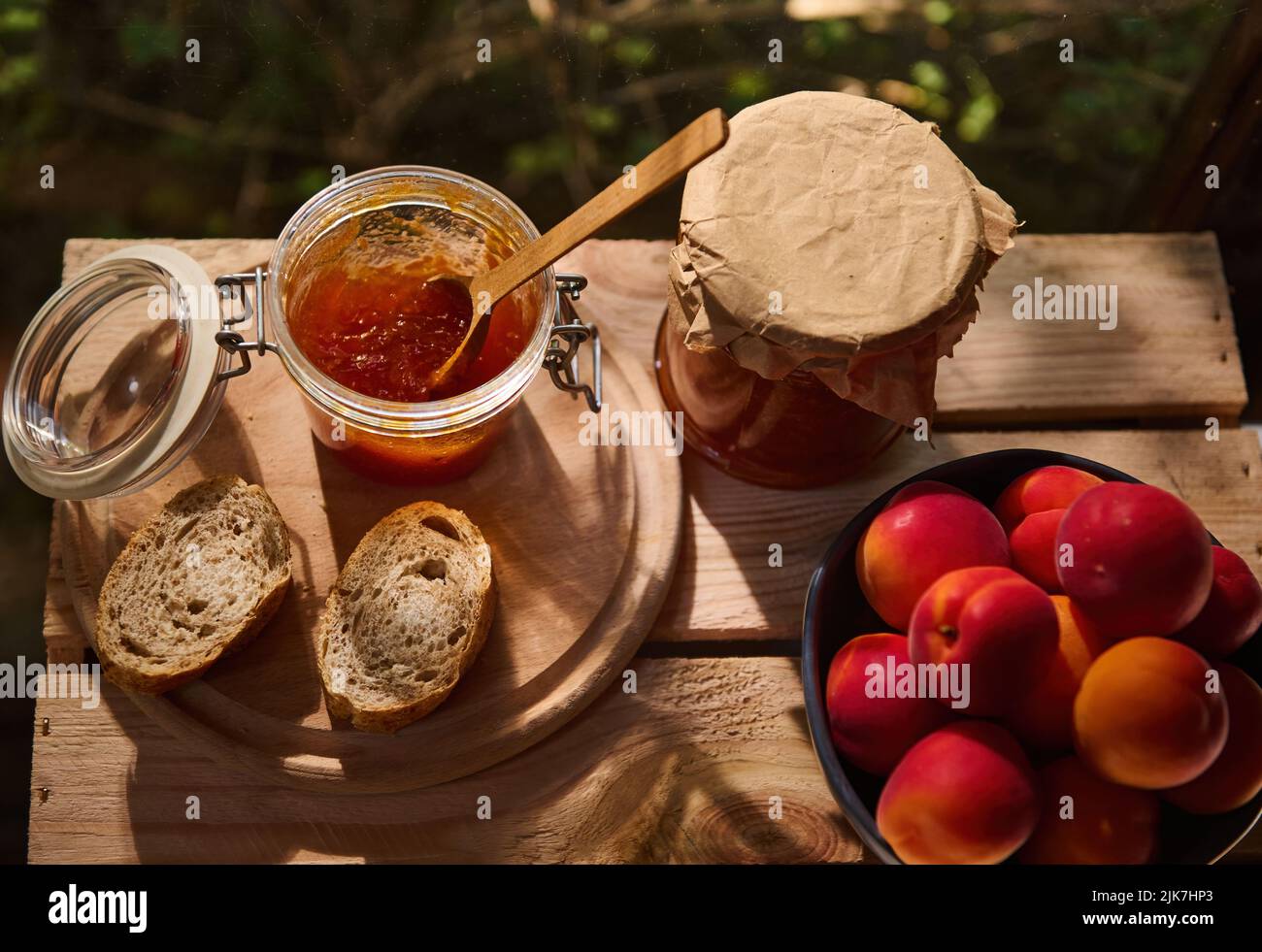 Hausgemachte Aprikosenmarmelade in einem Glas mit einem Löffel, Scheiben Vollkornbrot auf einer Holzkiste. Landhausstil. Draufsicht Stockfoto