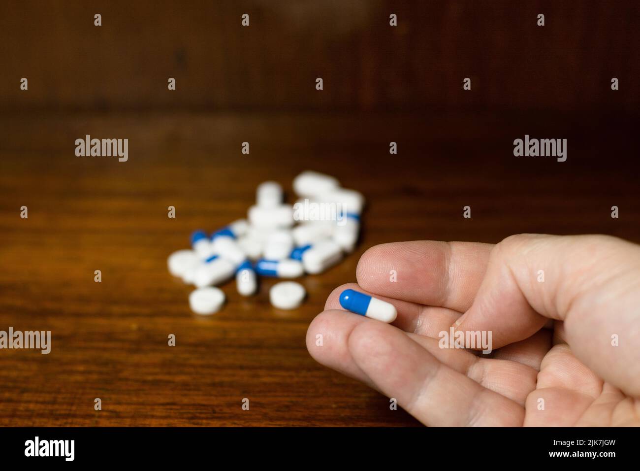 Einfacher Stapel weißer, blauer und gelber Pillen, Medikamente, Pillen auf braunem Hintergrund gestapelt. Finger der Hand mit einer blauen und weißen Pille. Stockfoto