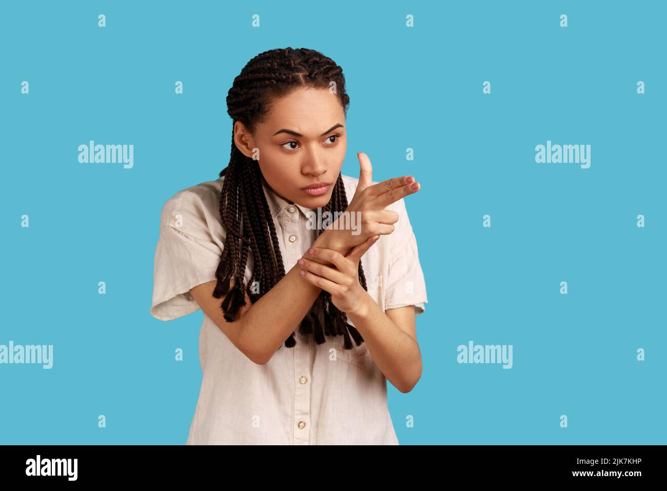 Portrait einer Frau mit schwarzen Dreadlocks, die mit einem Fingergewehr zeigen, mit Pistolenhandbewegung zielen und drohen, in einem weißen Hemd zu schießen. Innenaufnahme des Studios isoliert auf blauem Hintergrund. Stockfoto
