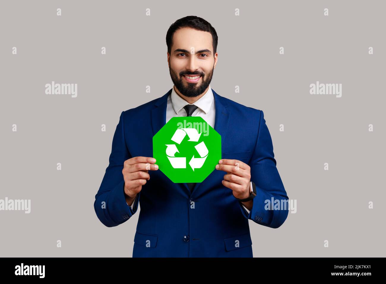 Positiv optimistischer bärtiger Geschäftsmann mit grünem Recycling-Zeichen, Umweltschutz, Ökologie-Konzept, im offiziellen Stil Anzug tragen. Innenaufnahme des Studios isoliert auf grauem Hintergrund. Stockfoto
