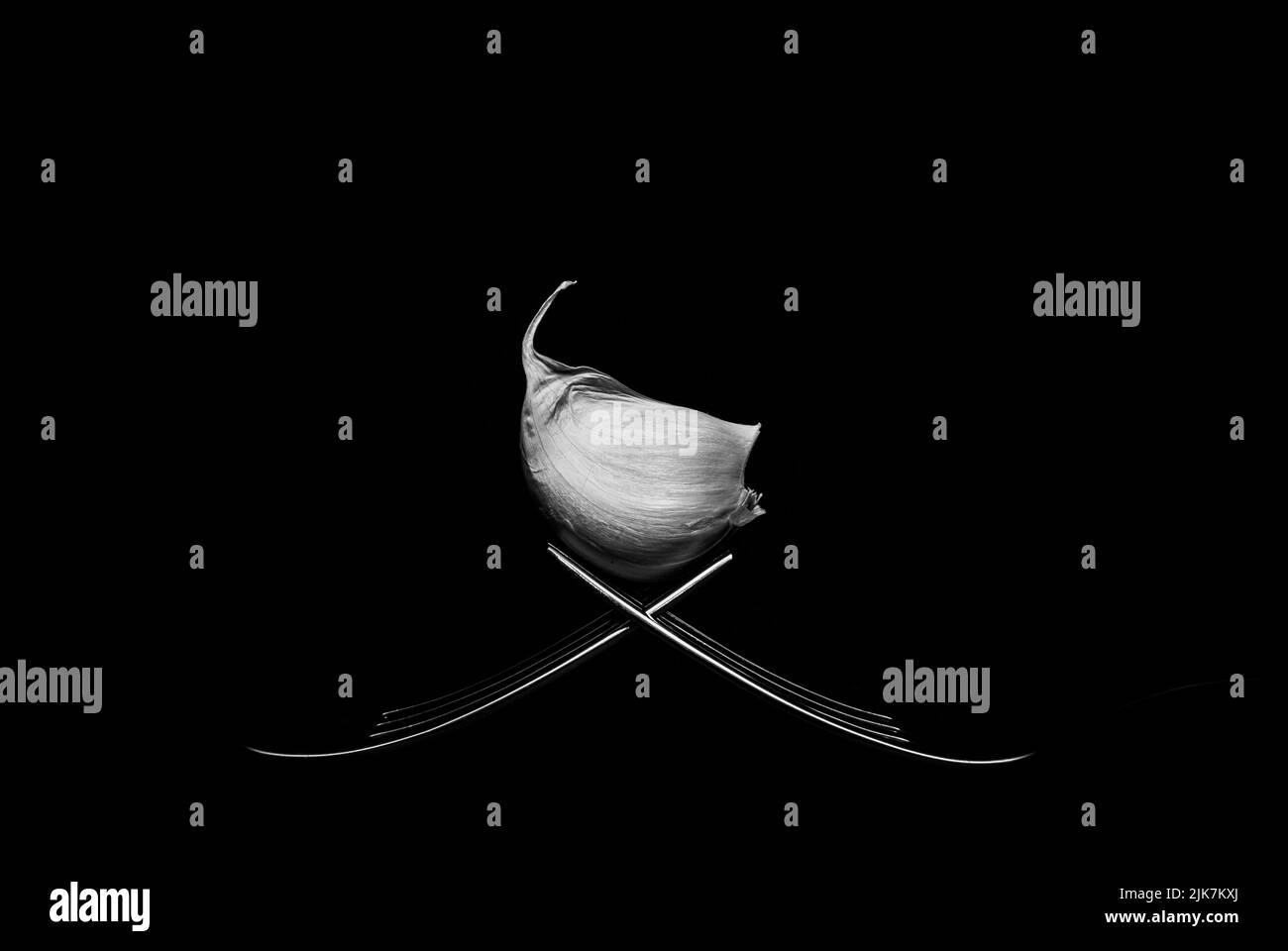 Low-Key-Bild einer Knoblauchzehe auf einem Paar Gabeln. Schwarz und Weiß. Stockfoto