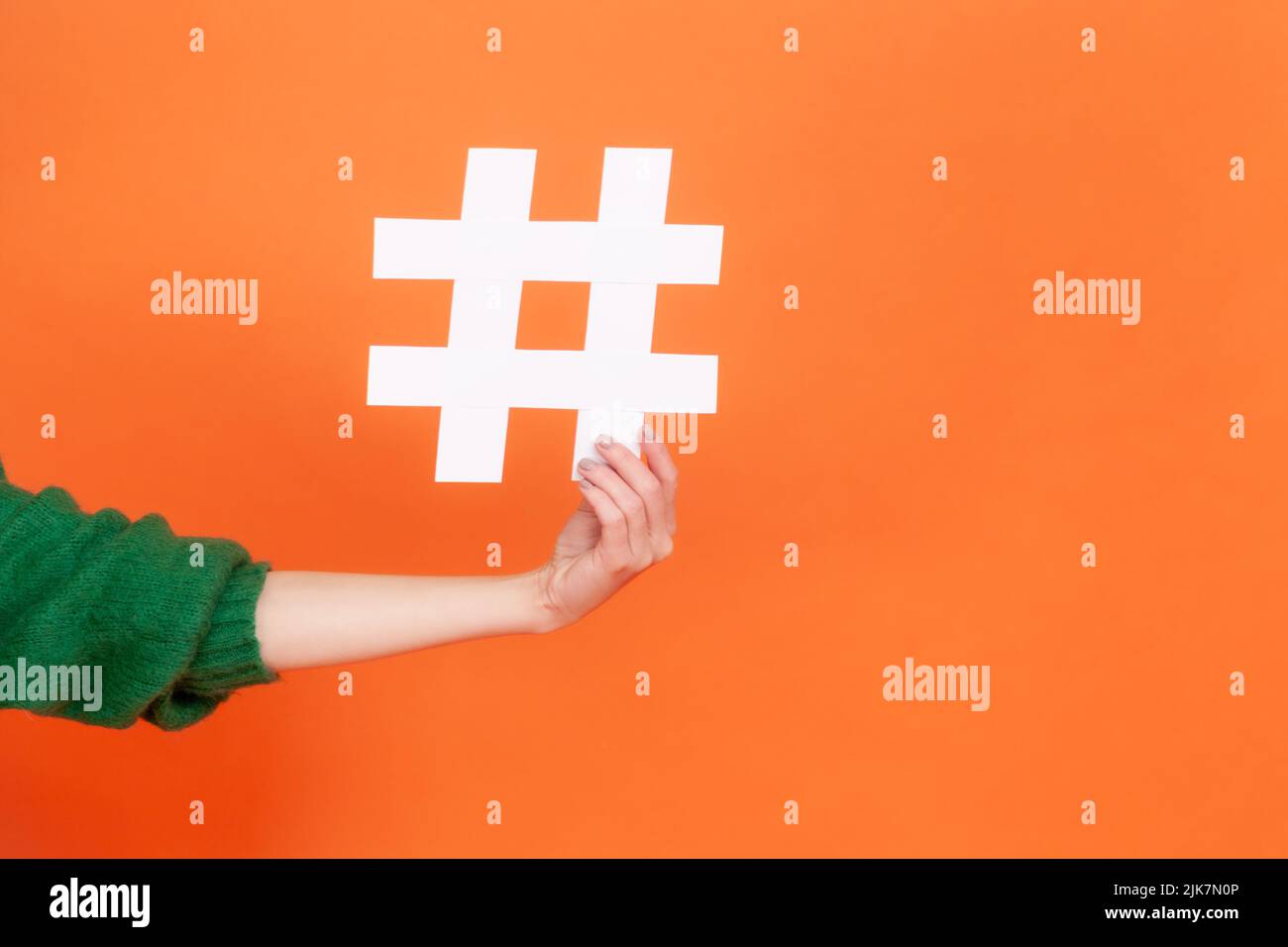 Nahaufnahme der Hand, die großes weißes Papier-Hashtag-Symbol neben dem Kopierraum hält, Hash-Zeichen für berühmte Medieninhalte, Social-Media-Marketing. Innenaufnahme des Studios isoliert auf orangefarbenem Hintergrund. Stockfoto