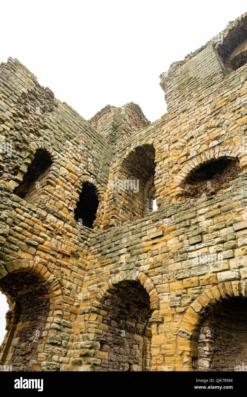 Dramatischer Blick nach oben auf die mittelalterlichen Burgmauern mit Steinbögen vor bedecktem Himmel Stockfoto