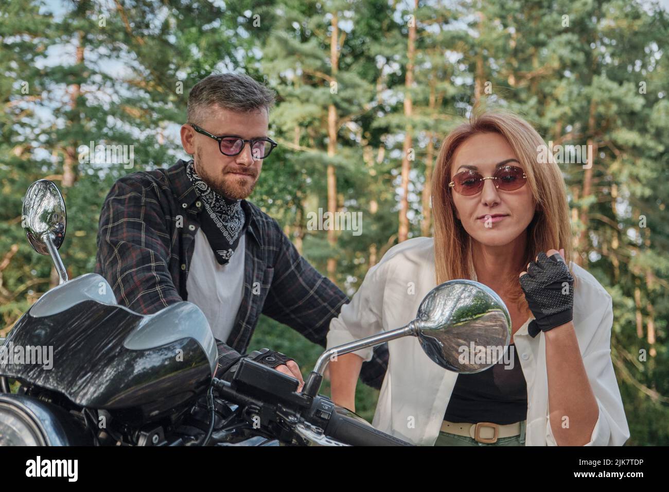 Eine Frau schaut in den Spiegel eines Motorrads, ein Paar mittleren Alters reist zusammen Stockfoto