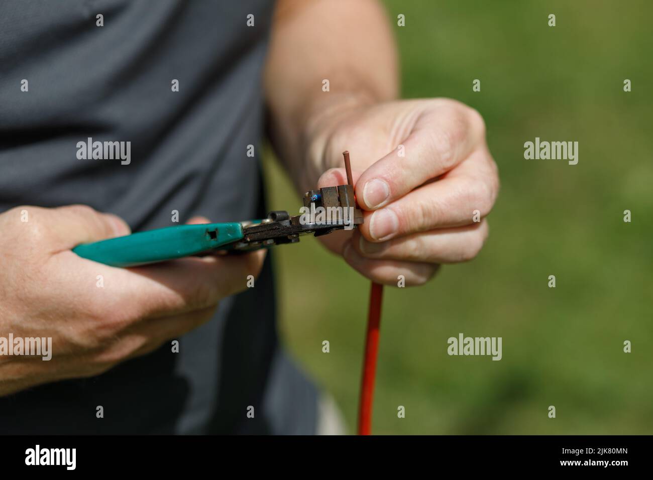 Drahtschneider, die in den Händen gehalten werden, um ein elektrisches Kabel zu schneiden Stockfoto