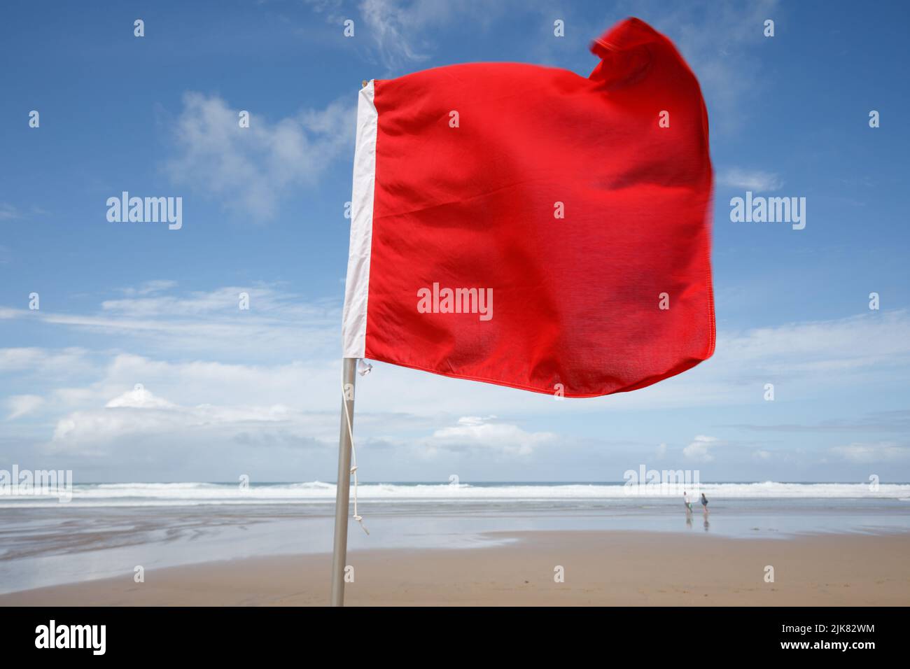 Rote Flagge am Strand. An einem windigen, aber sonnigen Sommertag weht eine rote Flagge im Wind, die Schwimmer vor gefährlichen Surfbedingungen warnt. Rote Flagge, Stockfoto