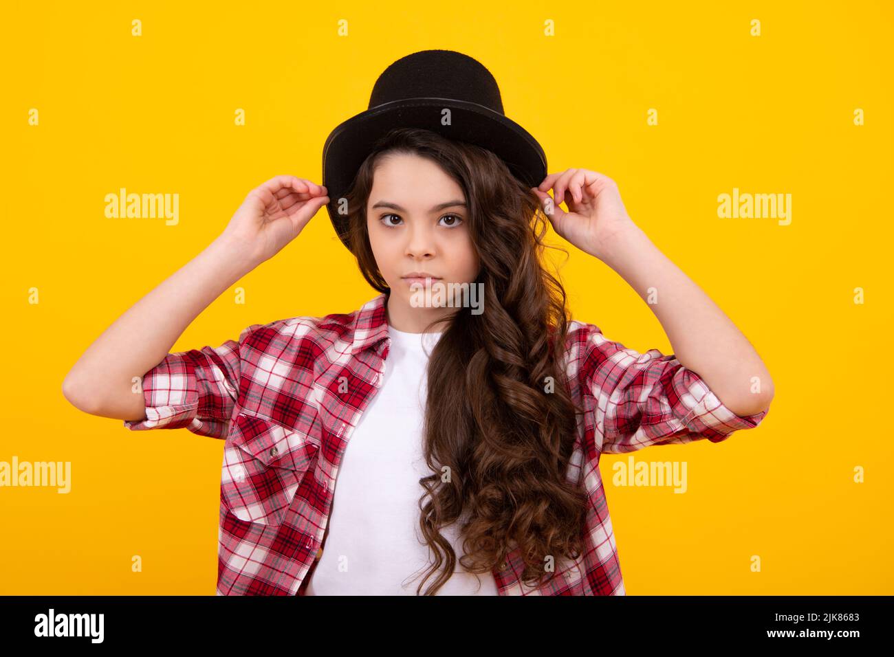 Kind Mädchen in Zauberer Hut, Zylinder Hut isoliert auf gelbem Hintergrund. Kopfbedeckung. Bekleidungszubehör. Modische Kopfbedeckungen für Herren im Vintage-Stil Stockfoto