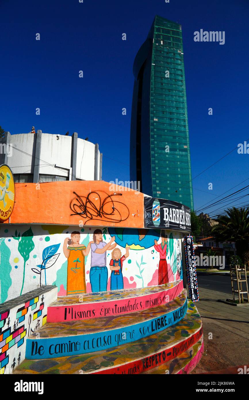 29.. Juni 2022, Av Ballivian, Calacoto, La Paz, Bolivien. Wandgemälde an der Wand eines Friseursalons im Bezirk Zona Sur von La Paz, gemalt von feministischen Gruppen, die Chancengleichheit und Rechte für Frauen fordern und gegen häusliche Gewalt und Gewalt gegen Frauen protestieren. Im Hintergrund befindet sich der Green Tower, der 2022 fertiggestellt wurde und mit 46 Etagen derzeit das höchste Gebäude Boliviens ist. Es handelt sich um ein Projekt und eine Investition der Compañía de Inversiones Comversa S.A. und des bolivianischen Geschäftsmannes und Politikers Samuel Doria Medina. Das Gebäude enthält sowohl Büros als auch Wohnungen. Stockfoto