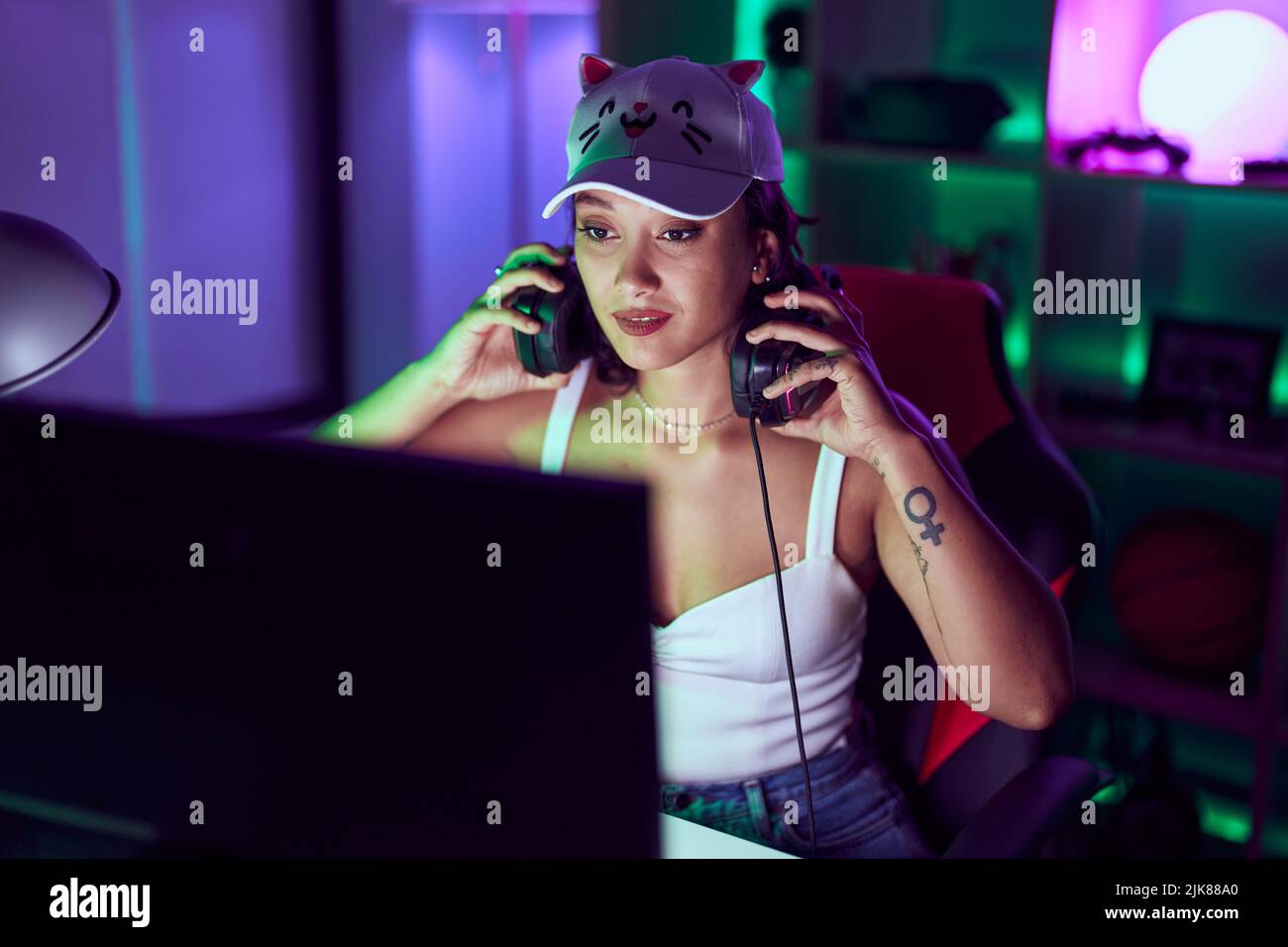 Junge schöne hispanische Frau streamer hält Kopfhörer im Spielzimmer Stockfoto