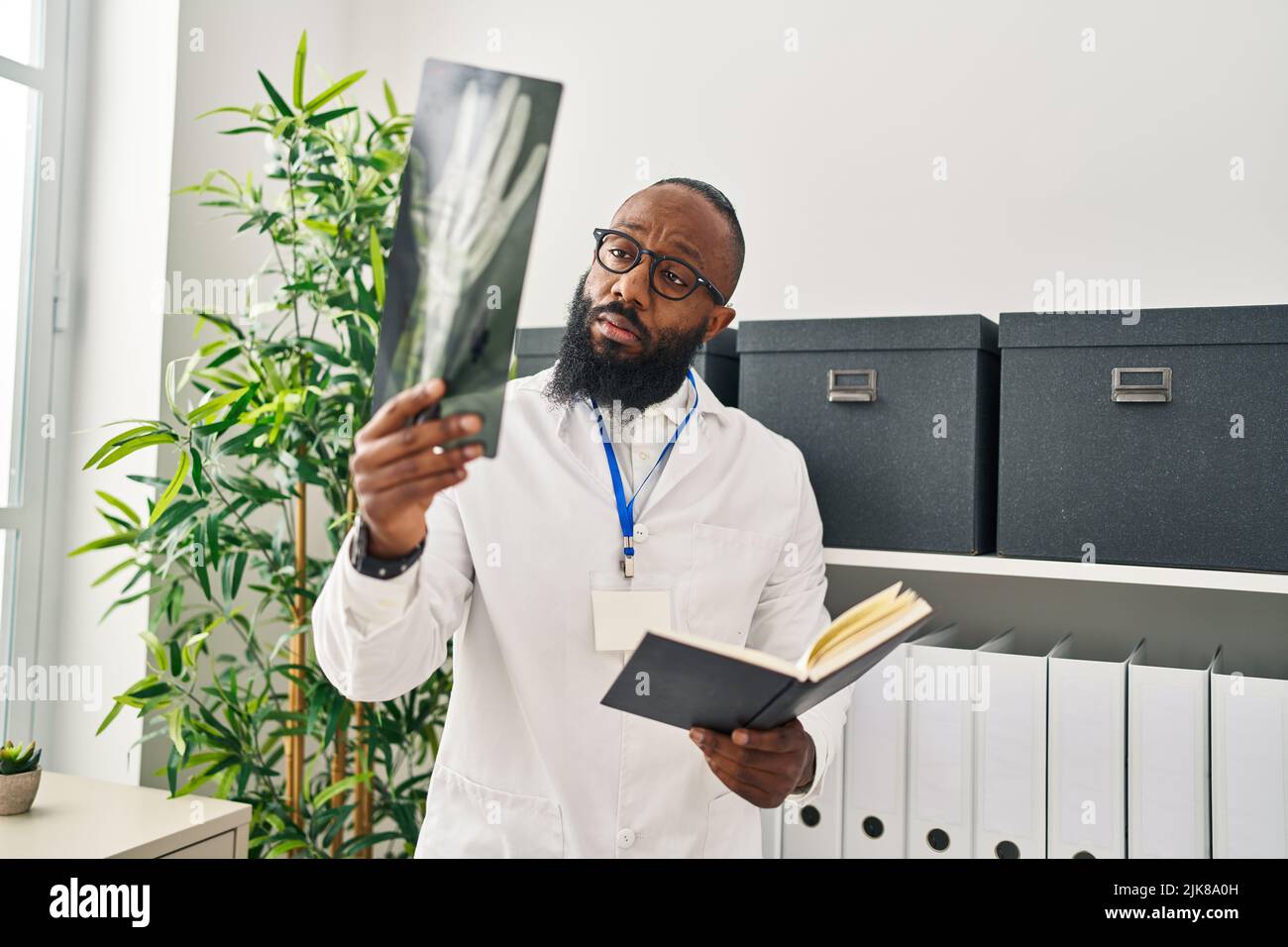 Junger afroamerikanischer Mann in Arztuniform, der Buch liest und in der Klinik Röntgenstrahlen sieht Stockfoto