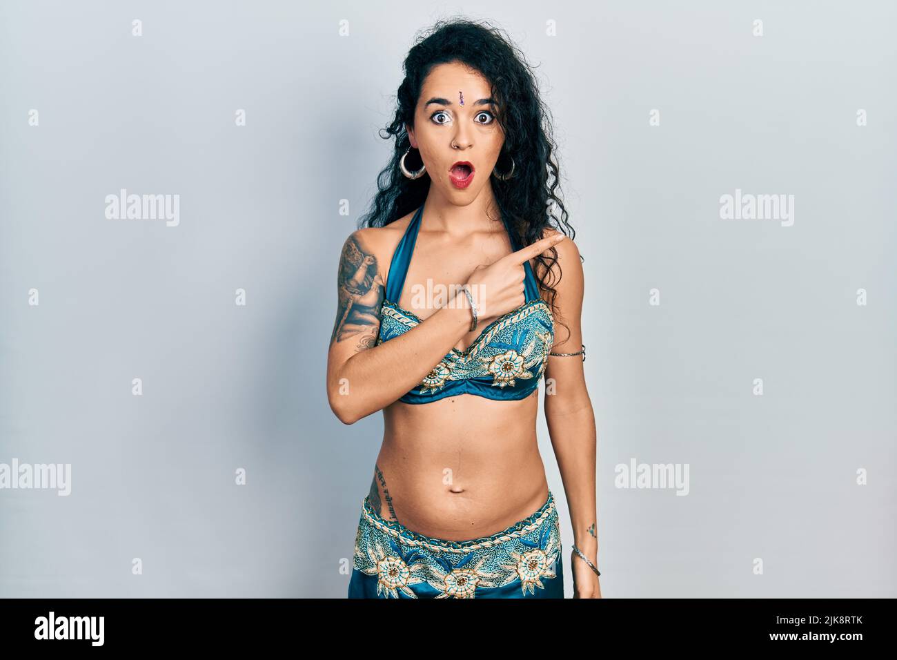 Junge Frau in Bindi- und traditionellen Bauchtanzkleidung überrascht, mit dem Finger zur Seite zeigend, offener Mund erstaunt Ausdruck. Stockfoto