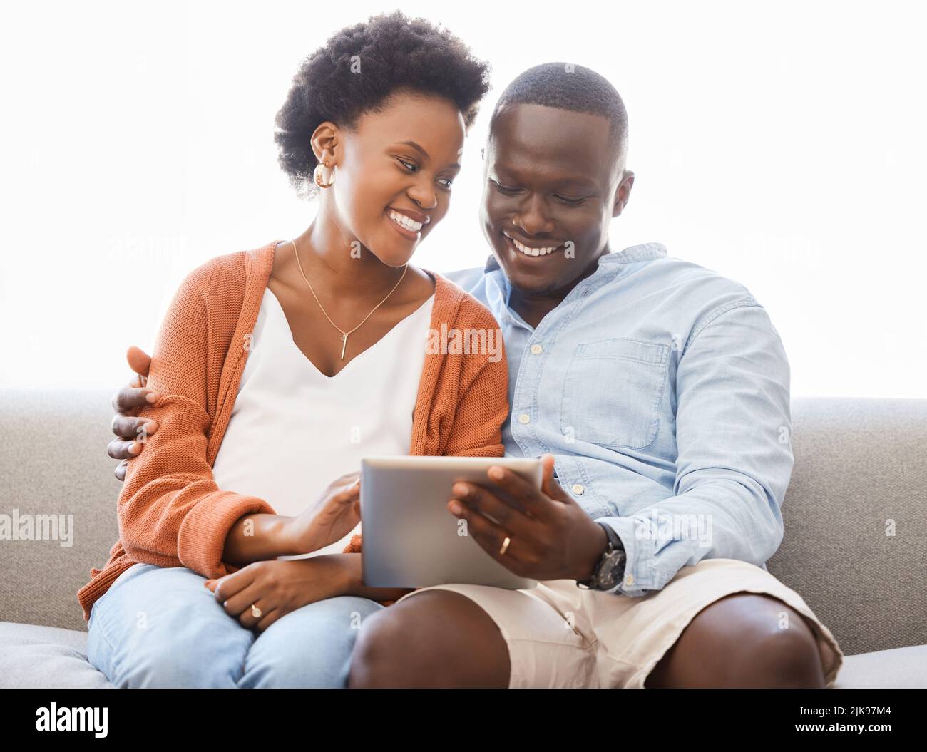 Auf der Suche nach einem neuen Zuhause. Ein junges Paar sitzt auf der Couch, während es zu Hause ein digitales Tablet benutzt. Stockfoto