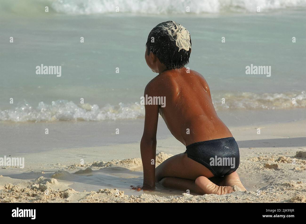 An einem Sommertag wird ein nicht erkennbarer mexikanischer Teenager mit Sand im Haar am Meer gespielt Stockfoto