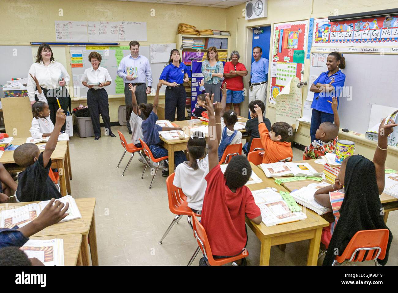 Miami Florida, Frederick Douglass Elementary School Hispanic Studenten jungen Schwarze Mädchen Klassenzimmer heben die Hände, Besucher von Anwaltskanzlei spenden Bücher Stockfoto