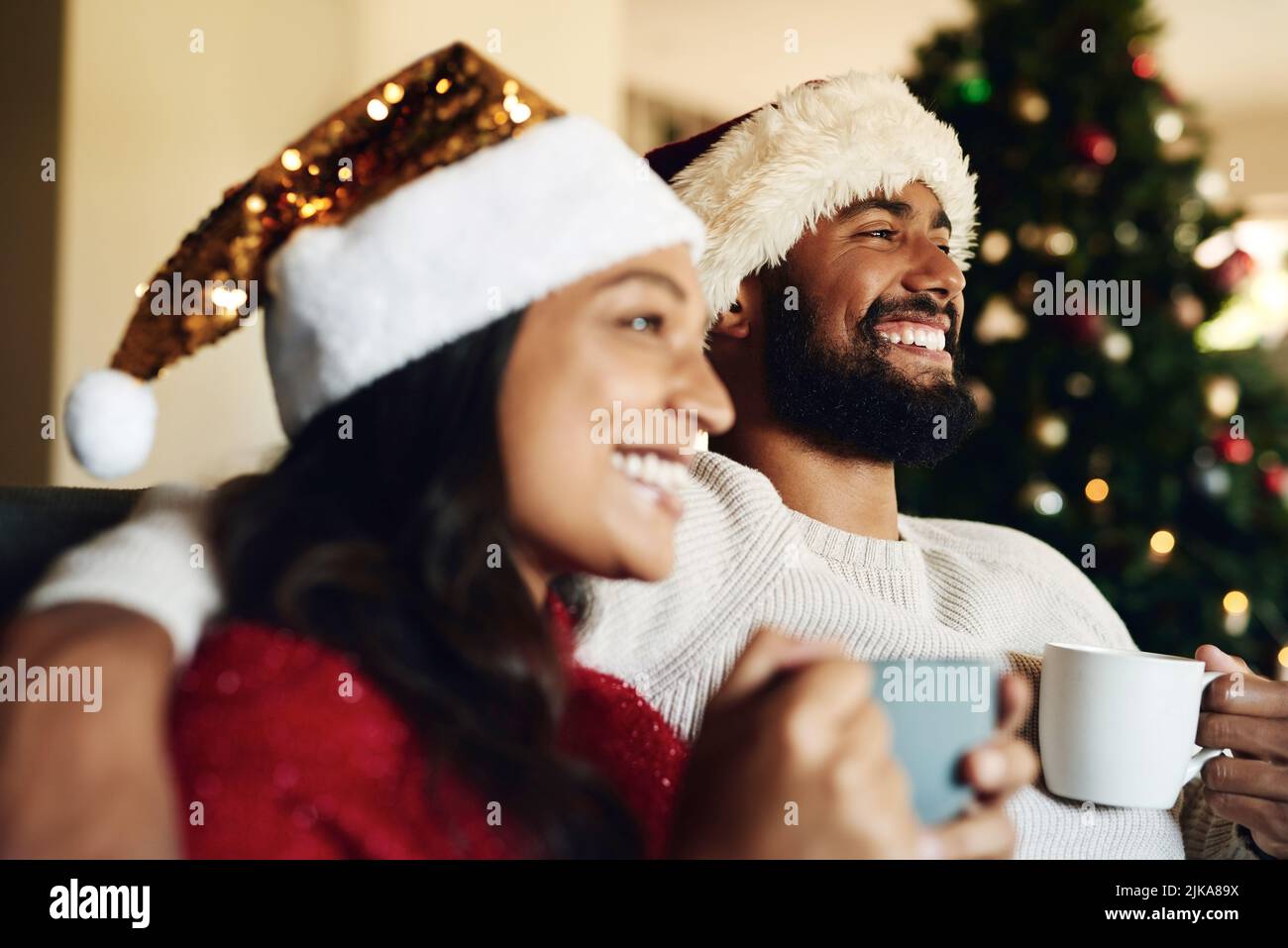 Bündeln Sie sich eng, seine Eiernacht. Ein glückliches junges Paar, das sich auf dem Sofa entspannt und während der Weihnachtszeit zu Hause warme Getränke trinkt. Stockfoto