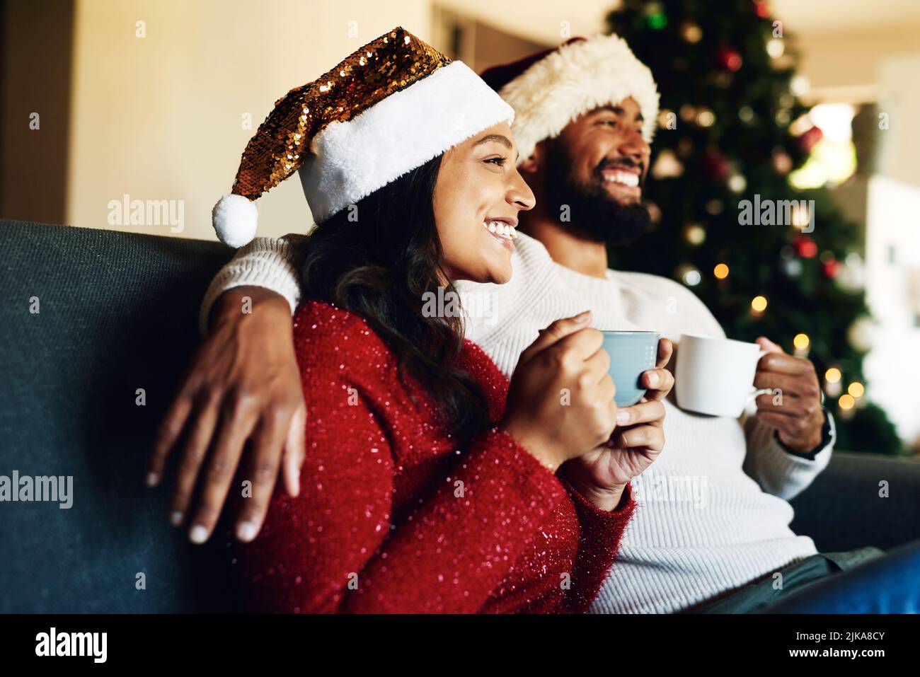 Heiße Schokolade und frohe Weihnachtserinnerungen. Ein glückliches junges Paar, das sich zu Hause auf dem Sofa entspannt und zu Weihnachten warme Getränke trinkt. Stockfoto