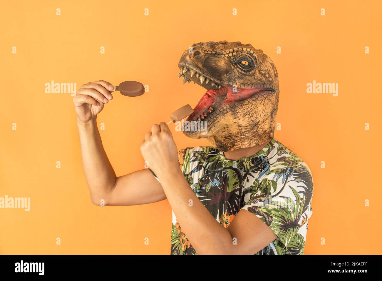 Mann in Dinosaurier Tier Kopf Maske essen zwei Schokolade Eis isoliert auf gelbem Hintergrund mit Kopierraum Stockfoto