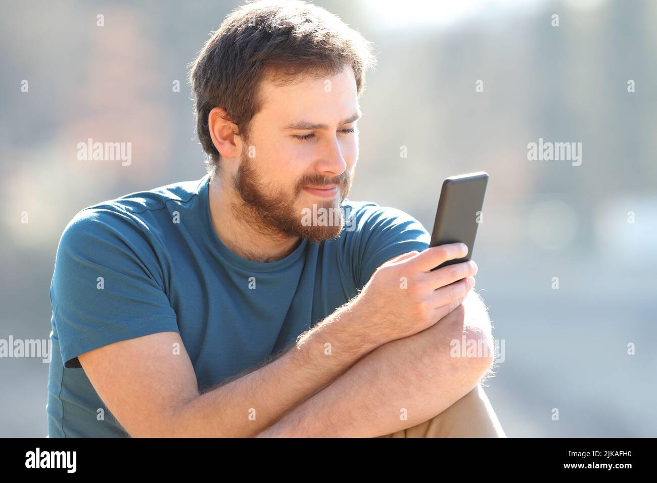 Zufriedener Mann beim Lesen von Handy-Inhalten im Freien Stockfoto