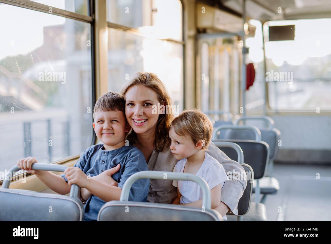 Junge Mutter mit kleinen Kindern, die im Sommer in der Straßenbahn unterwegs sind, pendeln und ein nachhaltiges Lifestyle-Konzept entwickeln. Stockfoto