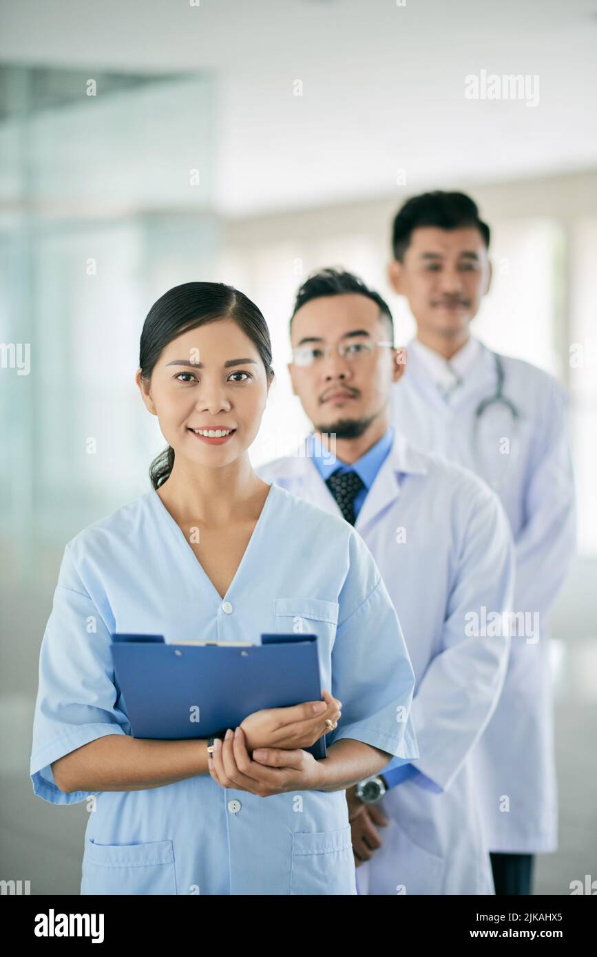 Lächelnde junge Ärztin und ihre männlichen Kollegen dahinter Stockfoto