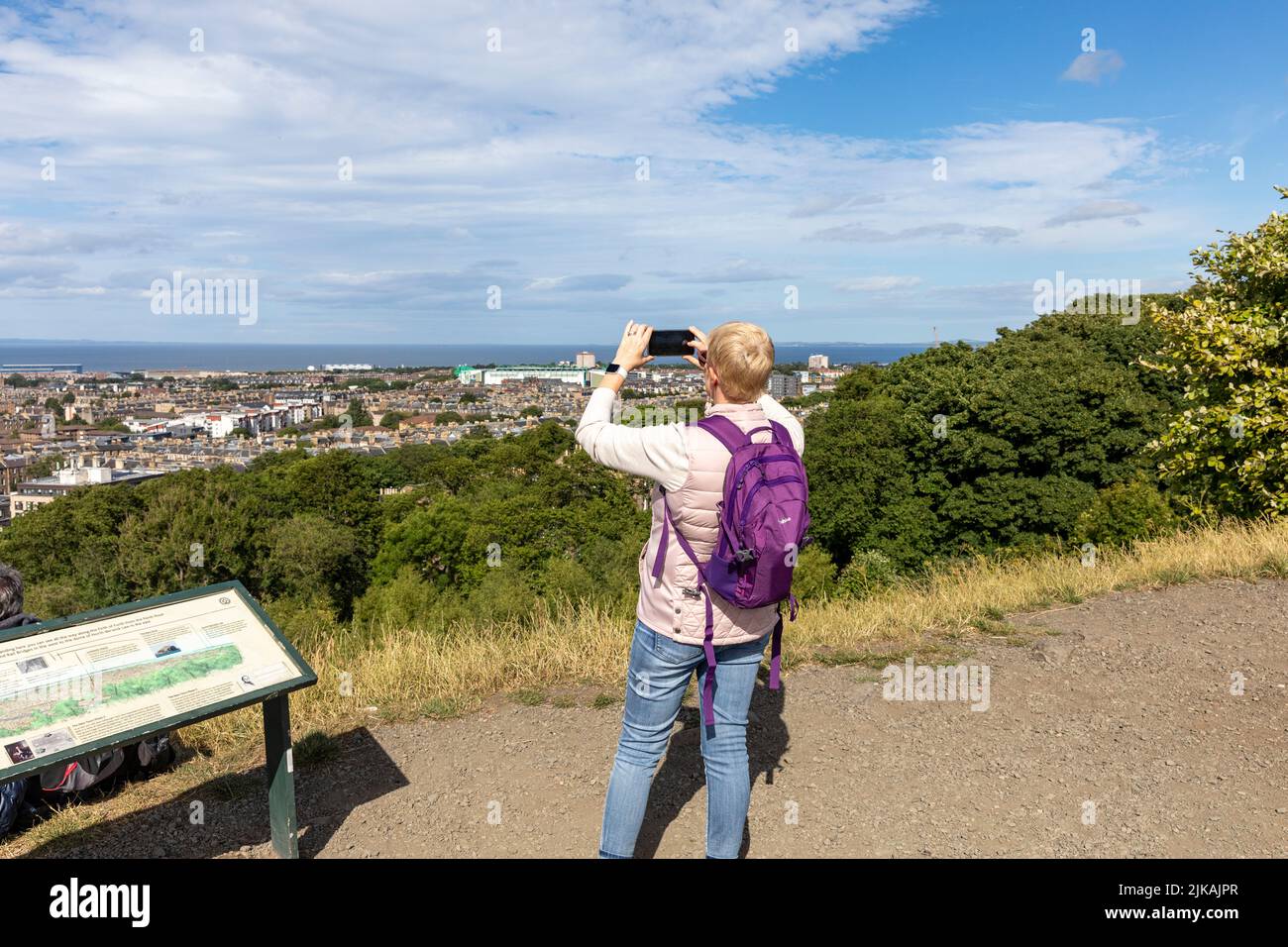 Edinburgh Calton Hill, Model veröffentlicht weibliche Tourist nutzt iPhone, um Edinburgh Stadtbild, blauer Himmel Sommer Tag, Schottland, Juli 2022 zu fotografieren Stockfoto