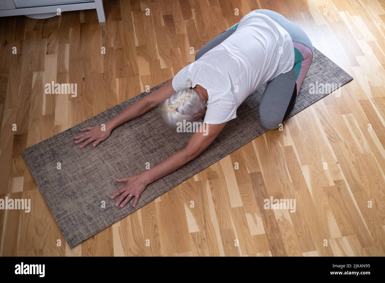 Frau kniet auf einer Matte und macht ein Balasana Asana, während sie zu Hause Yoga praktiziert Stockfoto