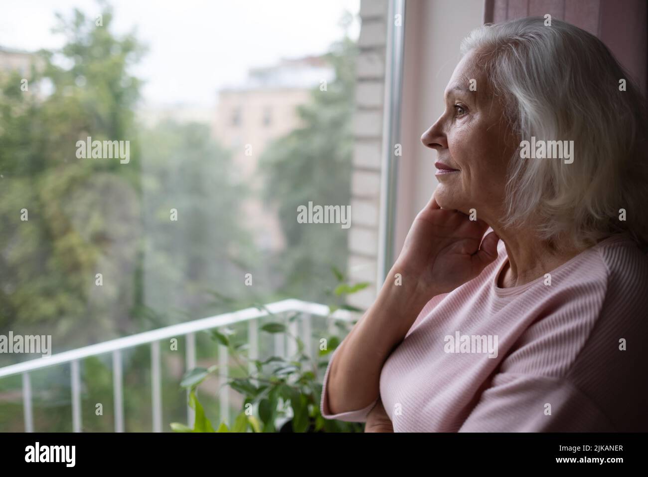 Eine ältere Frau sieht traurig aus dem Fenster. Stockfoto