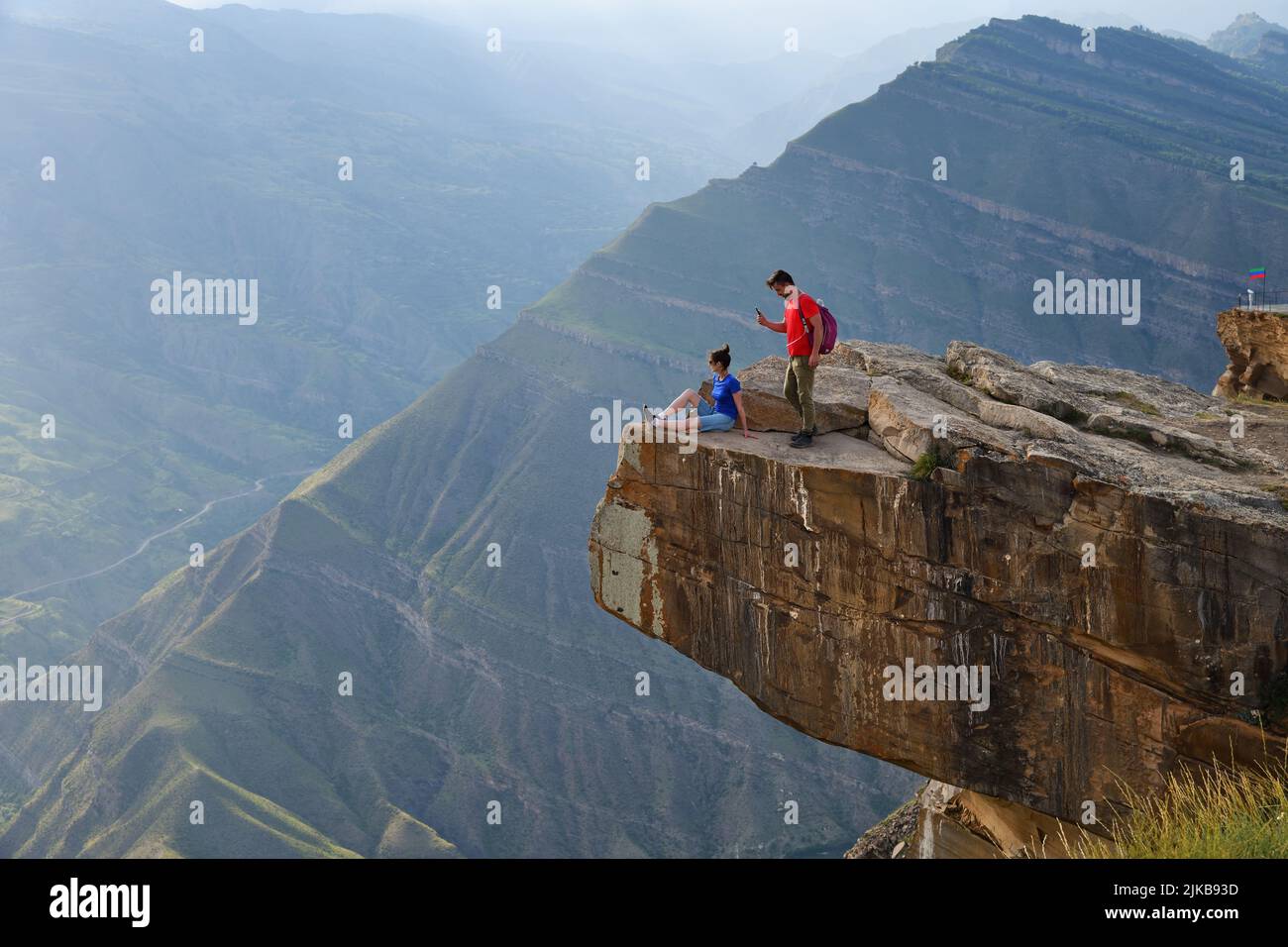 Dagestan, Russland - 21. Juli 2022: Junge Touristen am Rande der Klippe über dem tiefen Abgrund. Mann macht ein Handy-Foto oh seine Freundin. Leisten Stockfoto