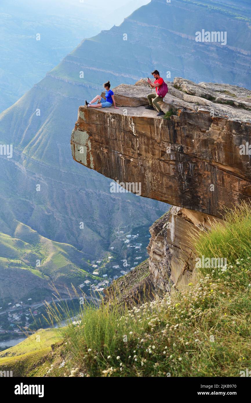 Dagestan, Russland - 21. Juli 2022: Junge Touristen am Rande der Klippe über dem tiefen Abgrund. Mann macht ein Handy-Foto oh seine Freundin. Leisten Stockfoto