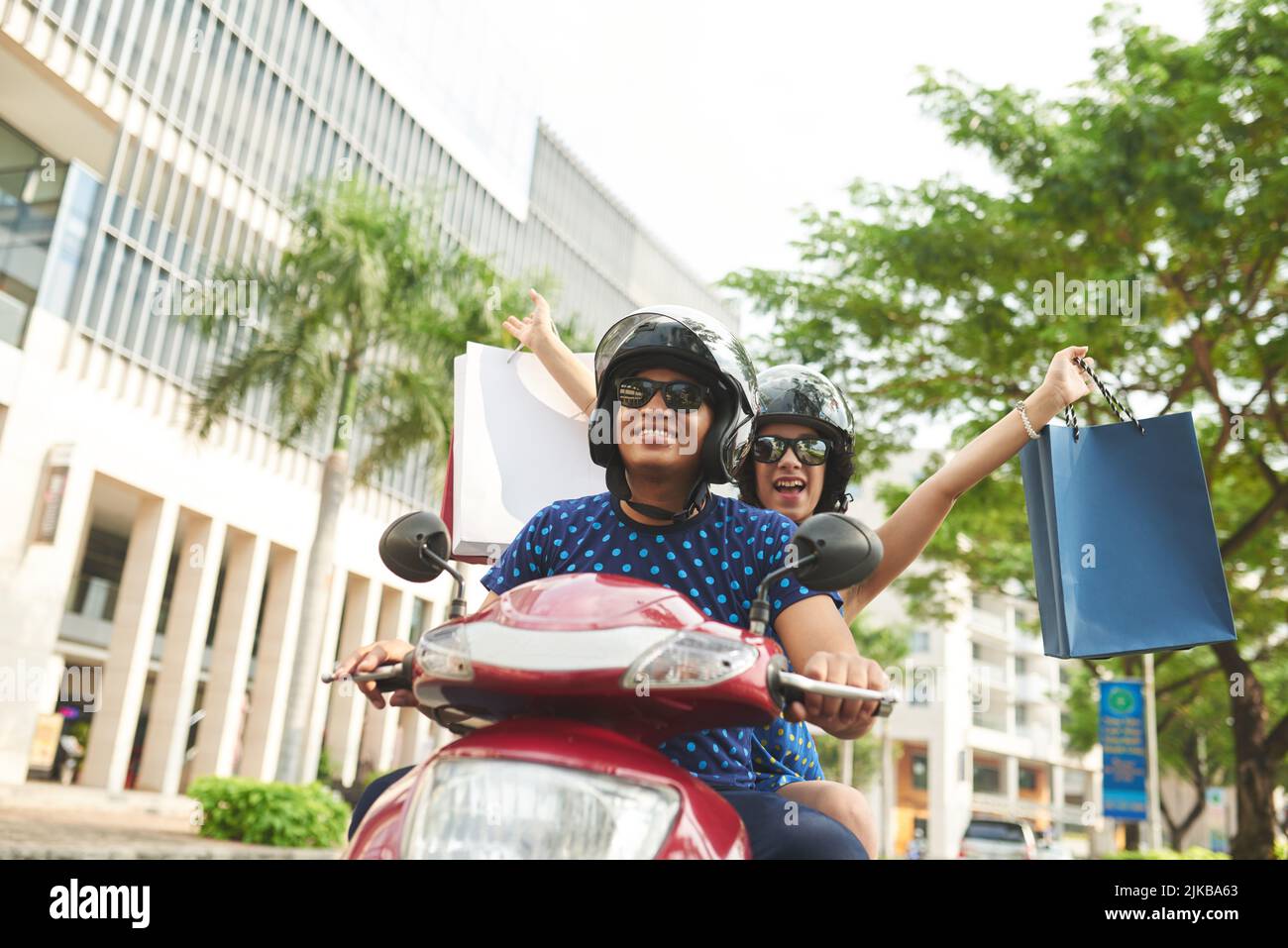 Glückliches lateinamerikanisches Paar mit Papiertüten, das auf einem Roller in der Stadt fährt Stockfoto